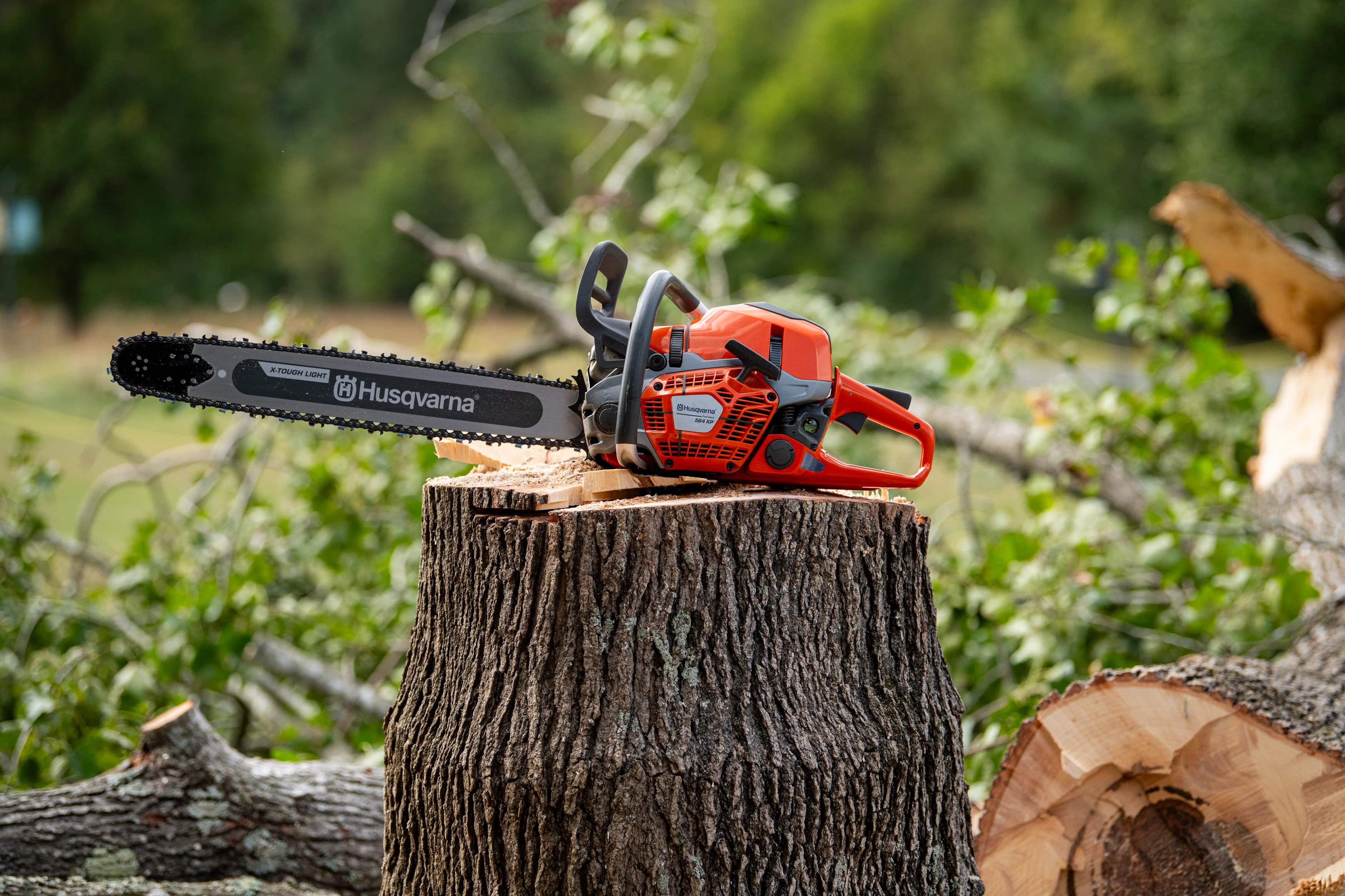 Husqvarna 564 XPG Fuel Inject Benzin-Motorsäge steht einsatzbereit auf einem Baumstumpf im Wald.