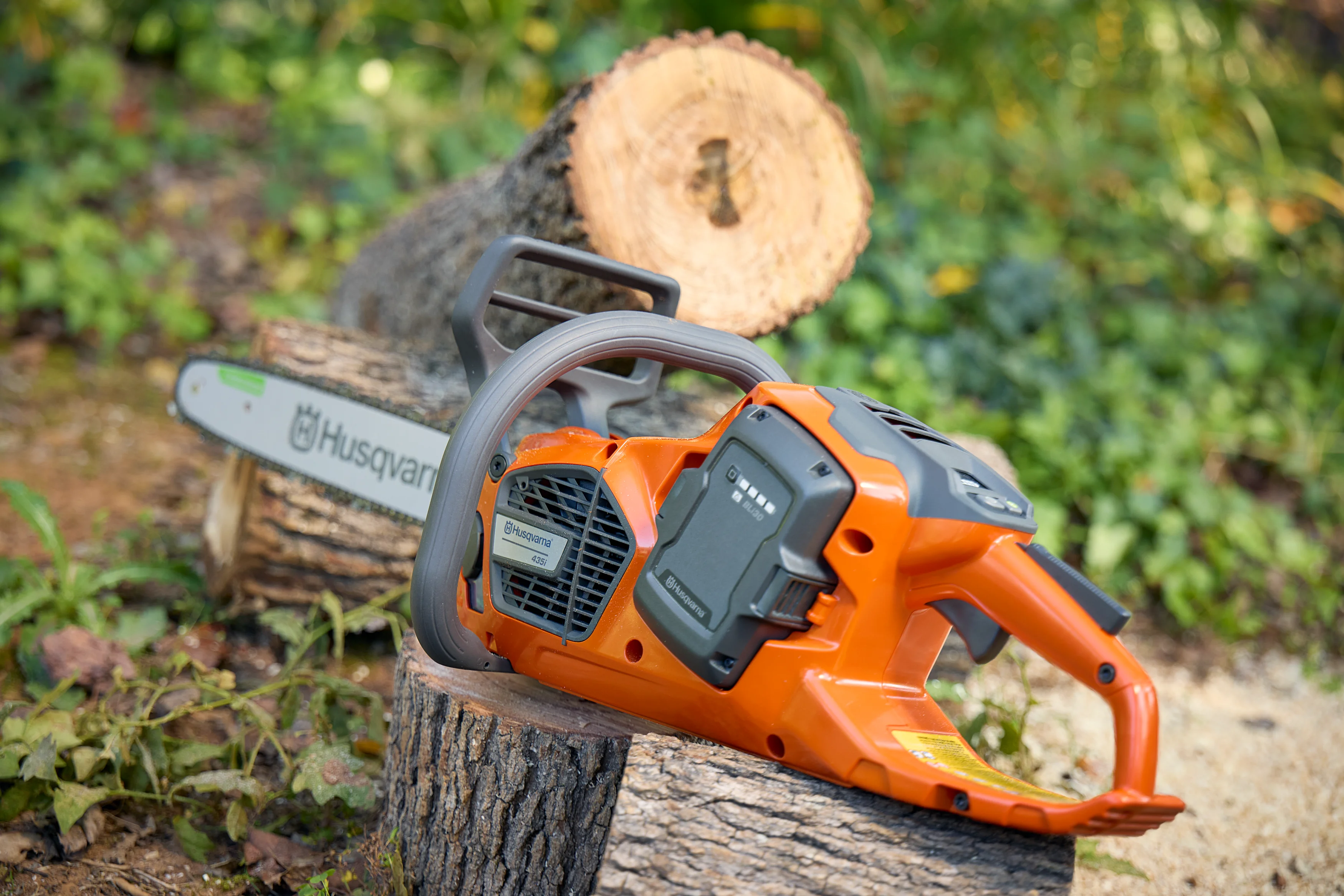 Husqvarna 435i Akku-Motorsäge mit eingesetztem Akku liegt auf einem Holzstamm.