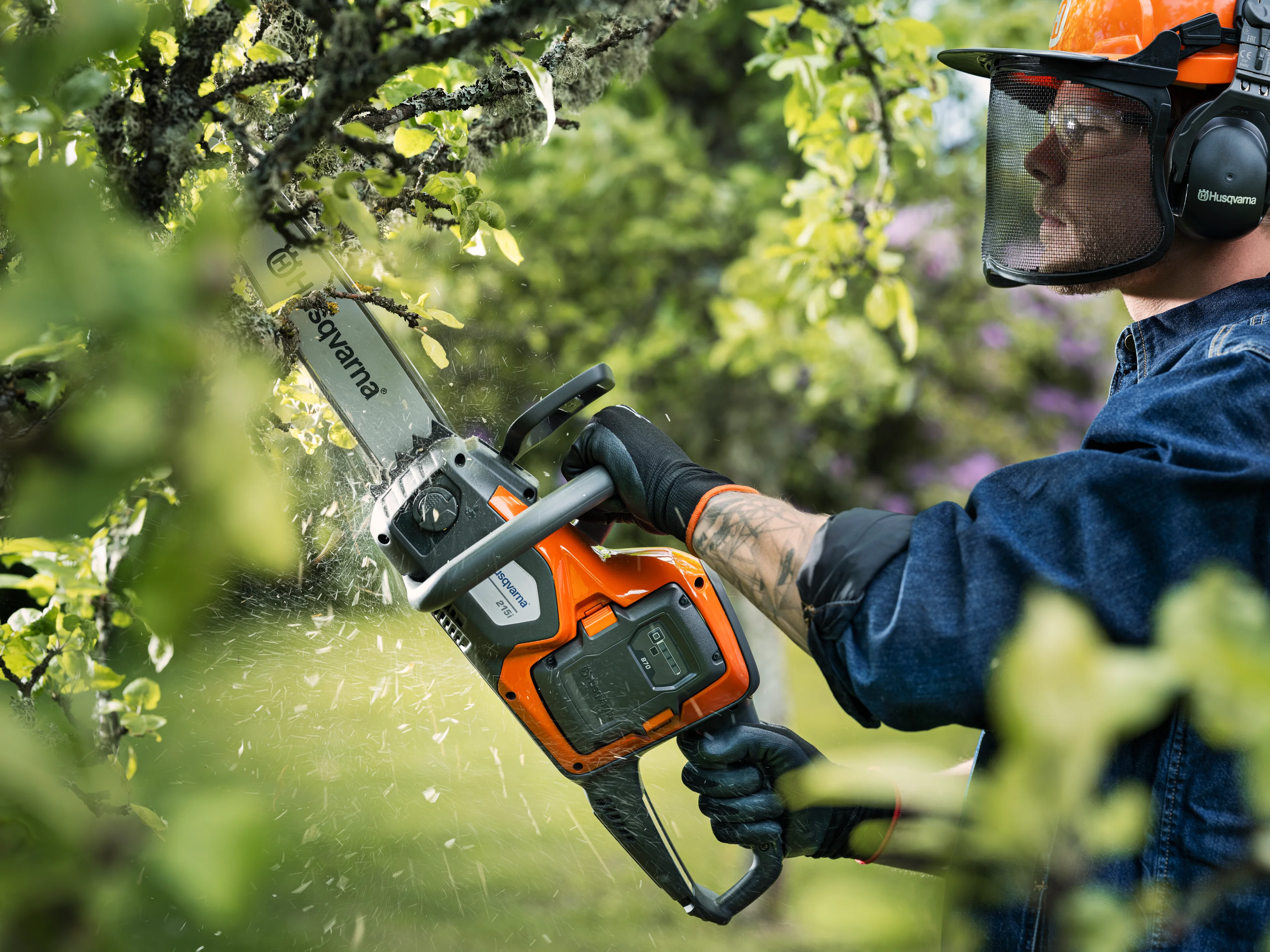 Waldarbeiter mit Helm und Schutzbrille schneidet mit der Husqvarna 215i Akku-Motorsäge Äste an einem Baum.