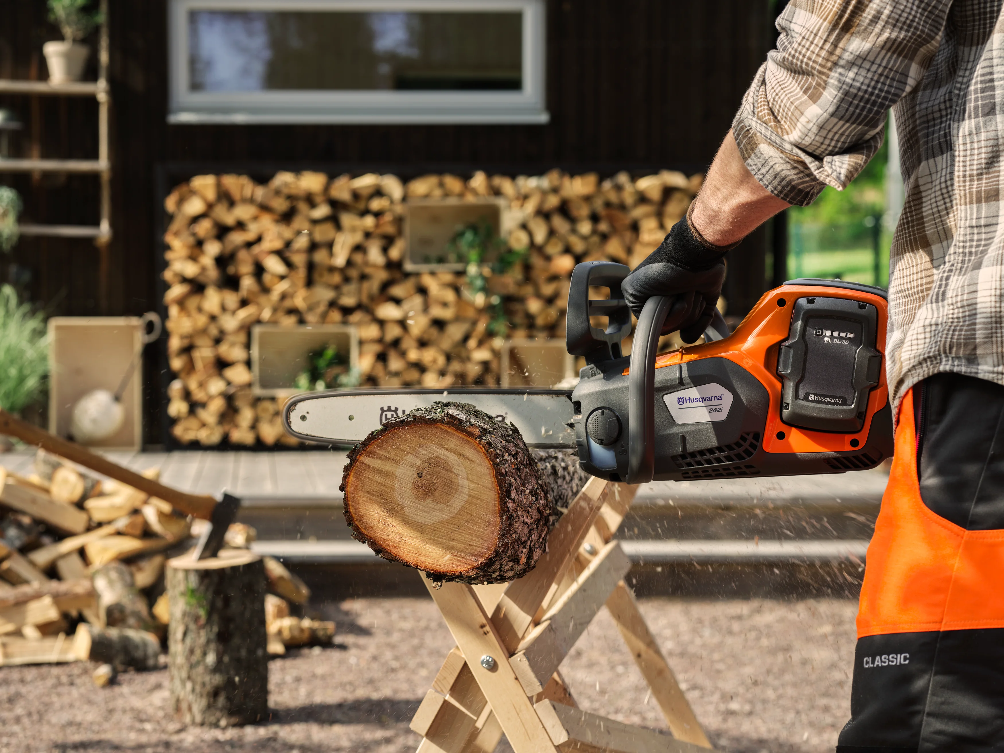Anwender in Schnittschutzhose sägt mit der Husqvarna 242i Akku-Motorsäge ein Holzscheit auf einem Sägebock.