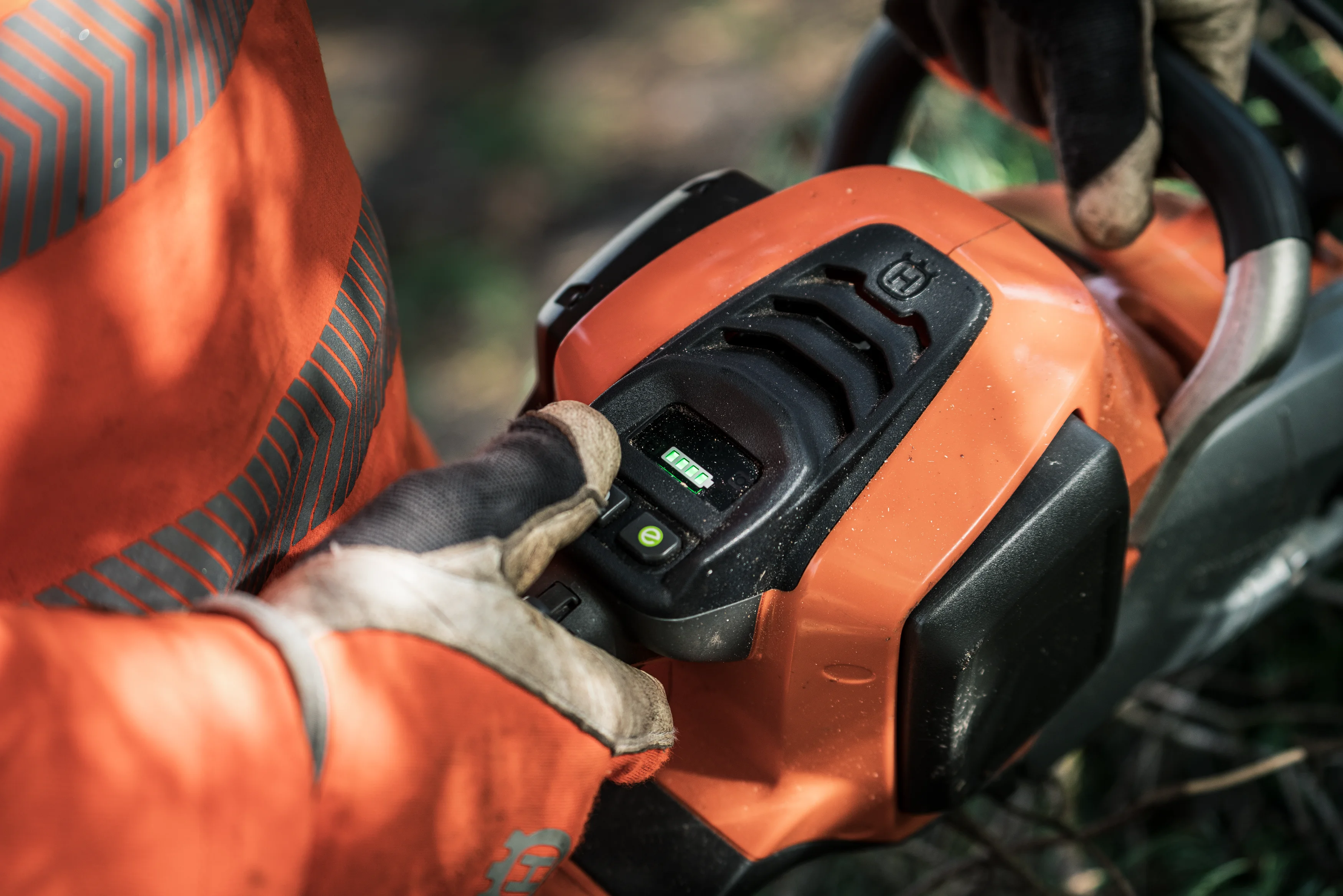 Anwender bedient mit Arbeitshandschuhen das digitale Bedienfeld der Husqvarna 540i XP Akku-Motorsäge mit beleuchteter Akku-Ladeanzeige.