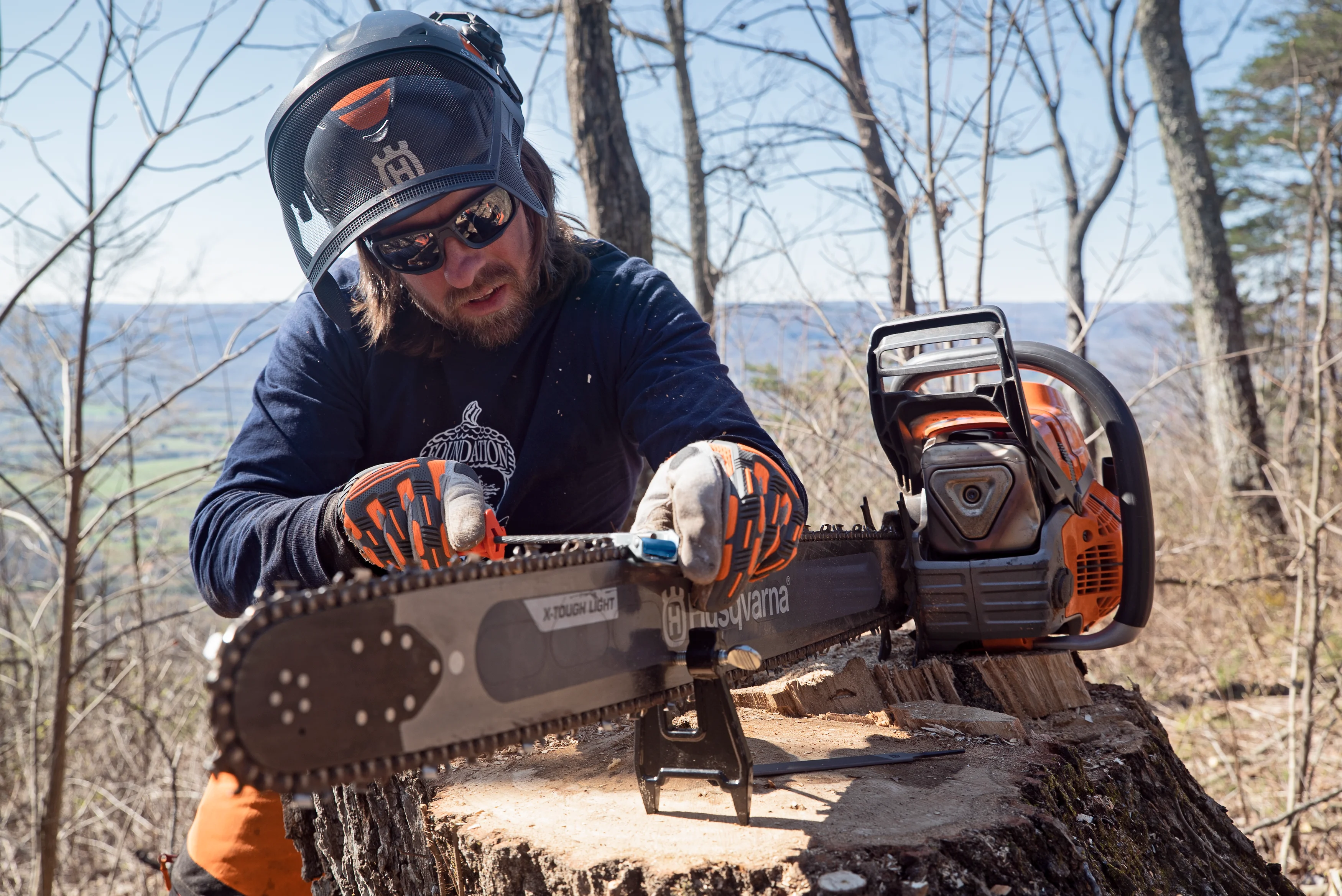Forstarbeiter schärft die Sägekette der Husqvarna 592 XP mit einer Feile auf einem Baumstumpf im Wald.